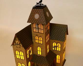 Peut inclure: Une maison hantée en papier kraft marron avec des fenêtres éclairées et une silhouette de corbeau noir sur le toit. La maison a un porche avec des balustrades et une porte d'entrée. Les fenêtres sont toutes éclairées d'une lueur jaune chaude.