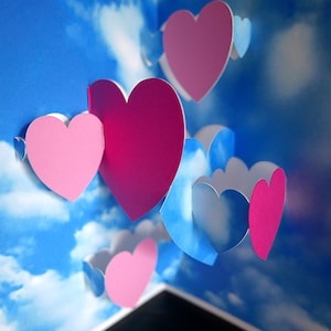 May include: A pop-up card with a blue sky and white clouds background. The card features multiple pink and red paper hearts in a 3D design.