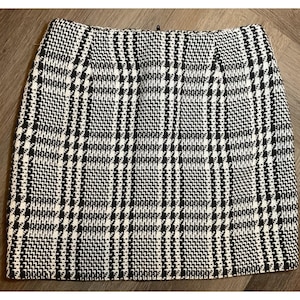 Peut inclure: Mini-jupe à motif pied-de-poule noir et blanc. La jupe présente un motif à carreaux classique avec une fermeture éclair. Le tissu semble être une matière tissée. La jupe est de couleur neutre et peut être associée à de nombreux hauts différents.
