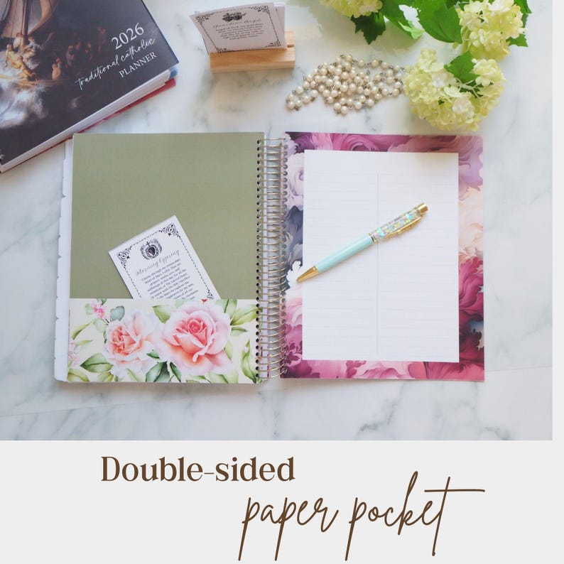 Pu&ograve; includere: Un'agenda a spirale aperta con una pagina verde salvia dotata di una tasca floreale contenente un piccolo biglietto, e una pagina destra con bordo floreale rosa e carta a righe. Una penna azzurra con punta dorata poggia sulla pagina a righe.