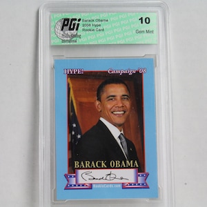 May include: A Barack Obama rookie card from the 2008 Hype! Campaign, graded Gem Mint 10 by Pristine Grading International. The card features a portrait of Obama and his signature, with the text "RookieCards.com".