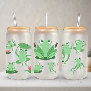 May include: Three frosted glass tumblers with bamboo lids and clear straws. Each tumbler features a different design of green frogs with various expressions. The designs include frogs on lily pads, frogs jumping, and frogs sitting on leaves.