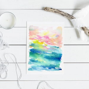 K&ouml;nnte beinhalten: Abstrakte Aquarellmalerei mit einem farbenfrohen Sonnenuntergang und einer Ozeanszene. Das Gem&auml;lde ist auf wei&szlig;em Hintergrund und in einem wei&szlig;en Passepartout gerahmt.