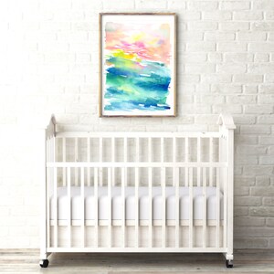 K&ouml;nnte beinhalten: Ein wei&szlig;es Babybett mit einer wei&szlig;en Matratze und einem gerahmten Aquarellbild mit abstrakten, bunten Pinselstrichen in Rosa-, Gelb-, Gr&uuml;n- und Blaut&ouml;nen, das an einer wei&szlig;en Backsteinwand h&auml;ngt.