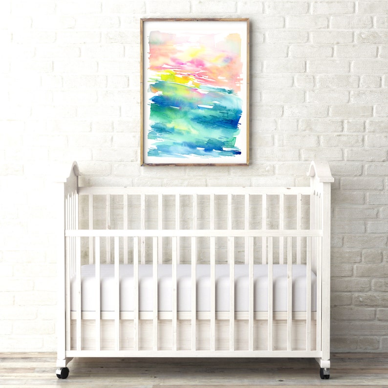 K&ouml;nnte beinhalten: Ein wei&szlig;es Babybett mit einer wei&szlig;en Matratze und einem gerahmten Aquarellbild mit abstrakten, bunten Pinselstrichen in Rosa-, Gelb-, Gr&uuml;n- und Blaut&ouml;nen, das an einer wei&szlig;en Backsteinwand h&auml;ngt.