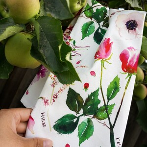 May include: White fabric with a watercolor floral print featuring roses, anemones, and berries. The fabric has the names of the flowers written in cursive on it: "Rose", "Anemone", and "Astilbe".