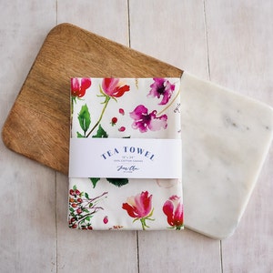 May include: A white tea towel with a floral pattern in shades of pink, red, and green. The towel is 18" x 24" and made of 100% cotton canvas. The text "TEA TOWEL 18" x 24" 100% COTTON CANVAS  Jane Chen" is printed on the towel.