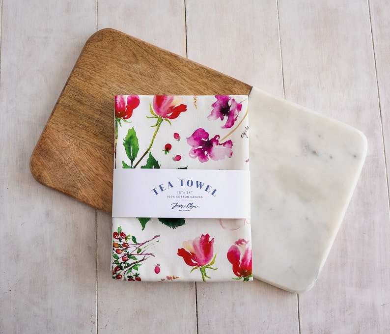 May include: A white tea towel with a floral pattern in shades of pink, red, and green. The towel is 18" x 24" and made of 100% cotton canvas. The text "TEA TOWEL 18" x 24" 100% COTTON CANVAS  Jane Chen" is printed on the towel.