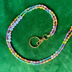 Puede incluir: Un cordón de cuentas de arcoíris con un cierre dorado y una etiqueta de nombre que dice "MRS. CELINE".