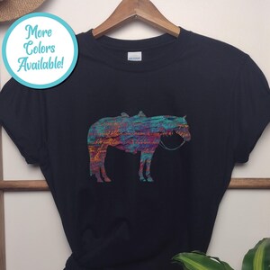 Op de afbeelding: Zwart T-shirt met een kleurrijk abstract paardenontwerp. Het paard is gesilhouetteerd en heeft een zadel en hoofdstel. De tekst "Meer kleuren beschikbaar!" staat in een blauwe cirkel.