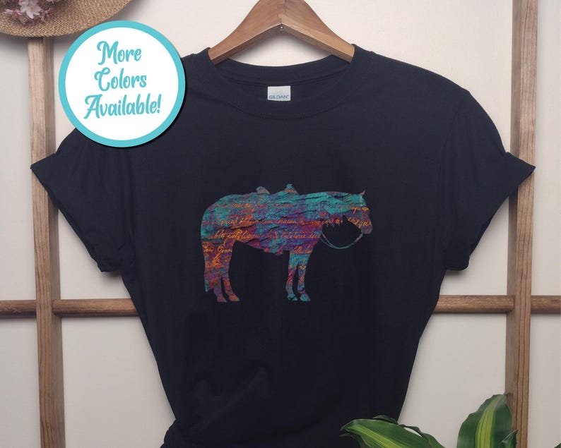 Op de afbeelding: Zwart T-shirt met een kleurrijk abstract paardenontwerp. Het paard is gesilhouetteerd en heeft een zadel en hoofdstel. De tekst "Meer kleuren beschikbaar!" staat in een blauwe cirkel.