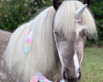 Può includere: Un pony grigio con criniera bianca e un corno da unicorno bianco fissato sulla fronte. La criniera è decorata con piume color pastello e il pony indossa un collare intrecciato dai toni pastello ornato con ulteriori piume.