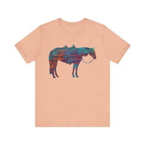 Op de afbeelding: Een lichtroze T-shirt met een kleurrijk silhouet van een paard met een zadel.