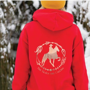 May include: Red hoodie with a rose gold graphic of a person riding a horse in a circle with the text "The Trails Are Calling".