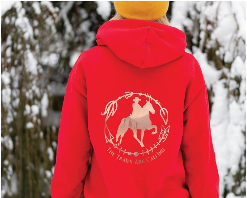 May include: Red hoodie with a rose gold graphic of a person riding a horse in a circle with the text "The Trails Are Calling".