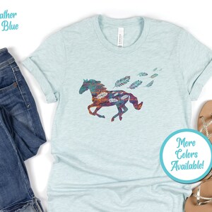 Peut inclure: Un t-shirt bleu glacier chin&eacute; avec une silhouette de cheval color&eacute;e et des plumes. Le texte "Plus de couleurs disponibles !" est sur un cercle bleu.
