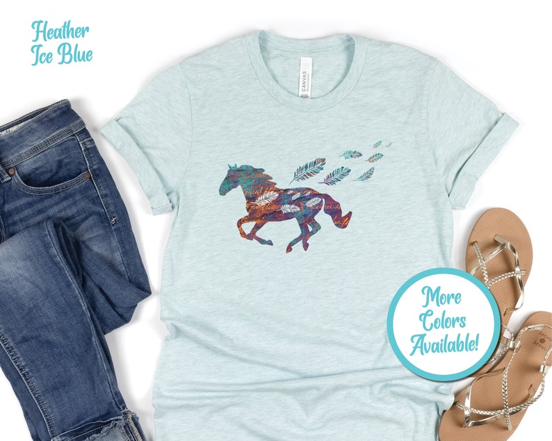 Peut inclure: Un t-shirt bleu glacier chin&eacute; avec une silhouette de cheval color&eacute;e et des plumes. Le texte "Plus de couleurs disponibles !" est sur un cercle bleu.