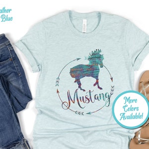 May include: A light blue t-shirt with a colorful graphic of a horse silhouette with the word "Mustang" and arrows. The text "More Colors Available!" is in a circle on the bottom right of the shirt.