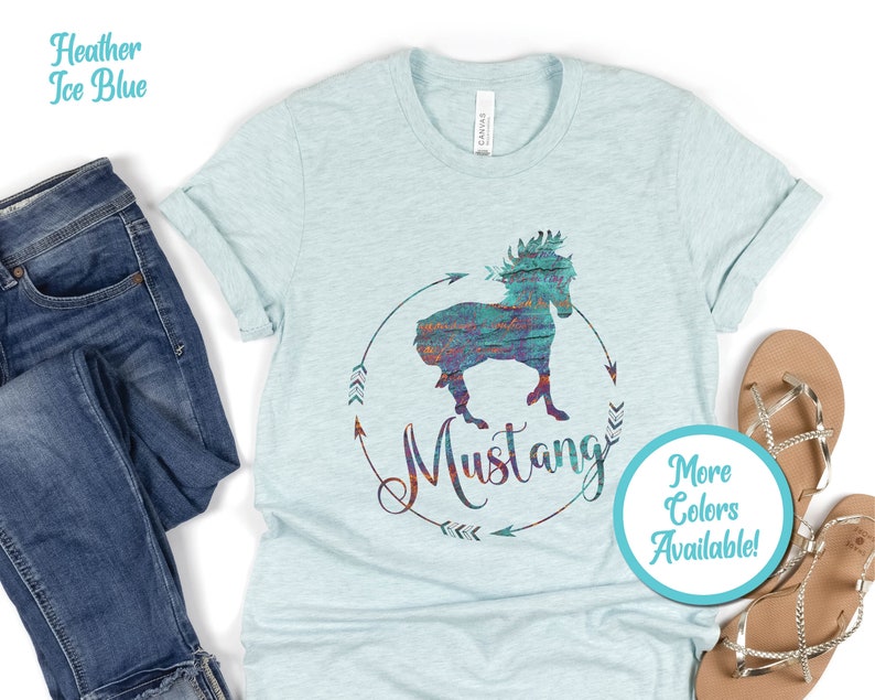 May include: A light blue t-shirt with a colorful graphic of a horse silhouette with the word "Mustang" and arrows. The text "More Colors Available!" is in a circle on the bottom right of the shirt.
