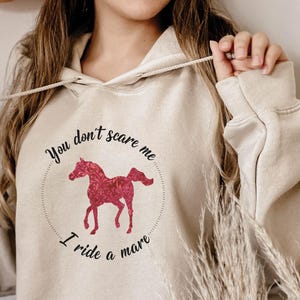 May include: A cream-colored hoodie with a pink horse graphic and the text "You don't scare me I ride a mare".