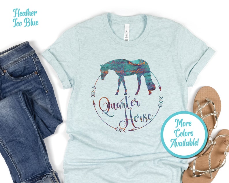 May include: A heather ice blue t-shirt with a graphic of a colorful quarter horse silhouette in a circle with the text "Quarter Horse" and arrows. The text "More Colors Available!" is in a circle below the graphic.