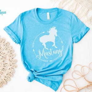 May include: A light blue t-shirt with a white silhouette of a horse and the word "Mustang" in a circle with arrows.