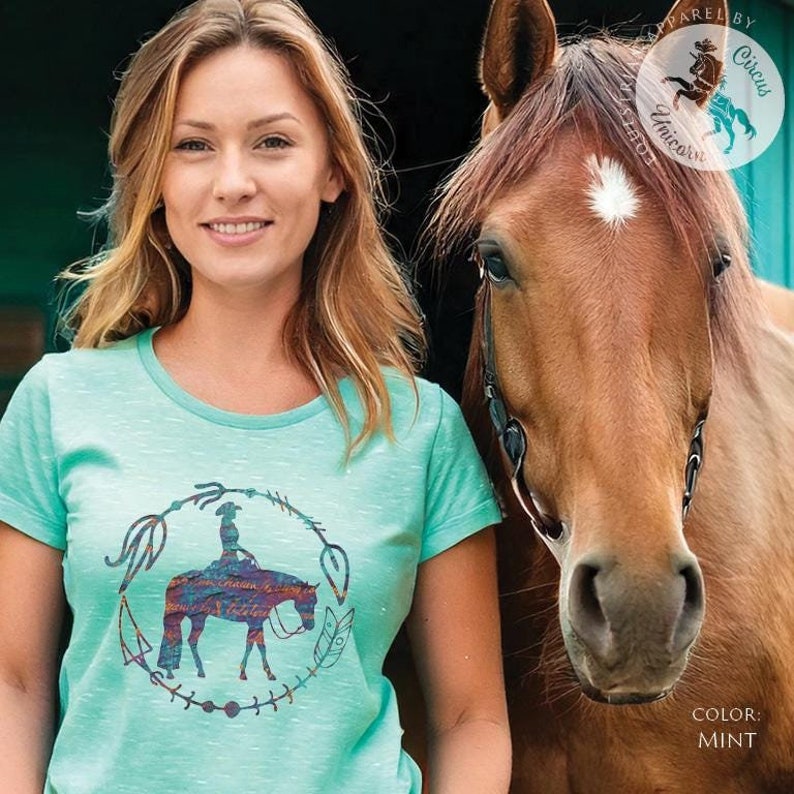 Pode incluir: Uma mulher vestindo uma camiseta verde menta com um gr&aacute;fico de um cavalo e um cavaleiro em um c&iacute;rculo com flechas e penas. O texto "Rarely by Circus Unicorns" &eacute; vis&iacute;vel no canto superior direito da imagem. As palavras "COLOR: MINT" s&atilde;o vis&iacute;veis no canto inferior direito da imagem.
