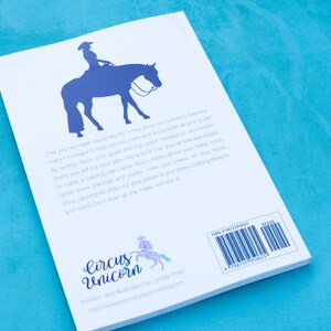 May include: A white book with a blue silhouette of a horse and rider on the cover. The back cover has the title "Circus Unicorn" and the text "Written and Illustrated by Lynda Phatt" and a website address. The book has a barcode and ISBN number.