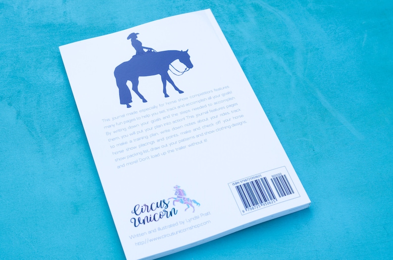 May include: A white book with a blue silhouette of a horse and rider on the cover. The back cover has the title "Circus Unicorn" and the text "Written and Illustrated by Lynda Phatt" and a website address. The book has a barcode and ISBN number.