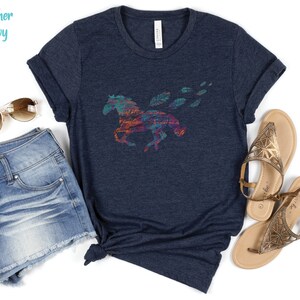 Peut inclure: Un t-shirt bleu marine chin&eacute; avec un motif de cheval abstrait color&eacute;. Le cheval court avec des plumes qui tra&icirc;nent derri&egrave;re lui.