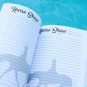 May include: An open notebook with the title "Horse Show" on the cover. The notebook has lined pages for writing notes and a silhouette of a rider on a horse on each page.