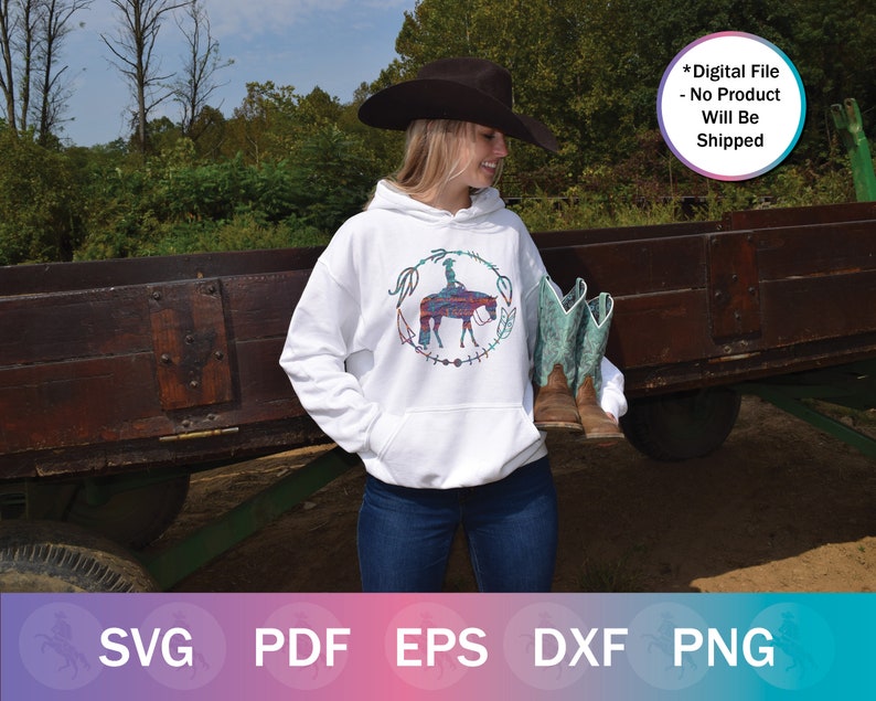 May include: White hoodie with a colorful graphic of a person riding a horse. The graphic is surrounded by a wreath of feathers and beads. The hoodie is being worn by a person wearing a black cowboy hat and blue jeans.