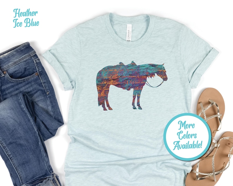 Op de afbeelding: Een hemelsblauw t-shirt met een kleurrijk silhouet van een paard. De tekst "Meer kleuren beschikbaar!" staat op een turquoise cirkel.