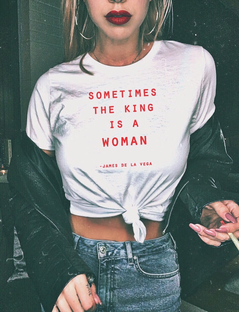 May include: White t-shirt with the text "Sometimes the king is a woman - James de la Vega" in red lettering.