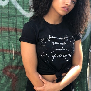 May include: A black t-shirt with a white graphic that says "be brave, baby girl you are made of stars" with a crescent moon and stars around the text.