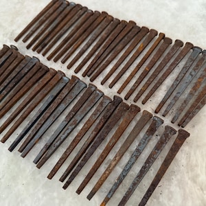 May include: A collection of antique, rusty nails with flat heads. The nails are arranged in rows, displaying a range of brown and gray tones, suggesting age and use. The image showcases a variety of sizes and shapes, suitable for woodworking or rustic decor.