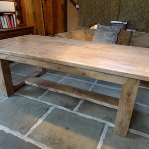 May include: A large, rustic wooden table with a thick, natural wood top and a simple, sturdy base. The table is made of reclaimed wood and has a natural, weathered finish.