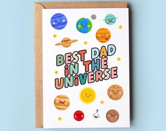 Puede incluir: Una tarjeta blanca con una ilustración colorida de planetas y estrellas. El texto "Best Dad in the Universe" está escrito en letras de arcoíris.