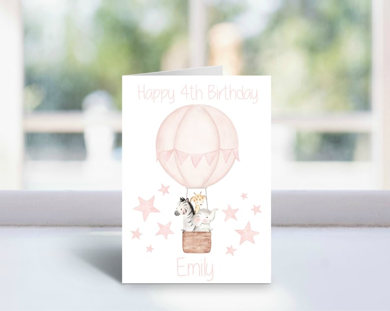 May include: Pink birthday card with a hot air balloon carrying a zebra, giraffe, and elephant. The balloon has pink and white bunting. The card says "Happy 4th Birthday" and "Emily".