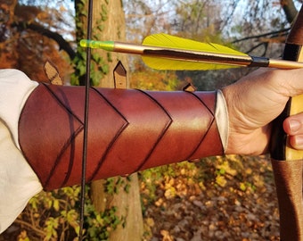 May include: A brown leather arm guard with decorative stitching and metal accents. The arm guard is worn on the left arm and is being used to protect the arm from a bowstring.