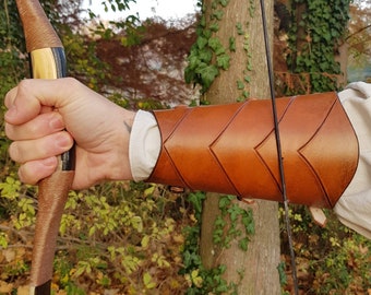 May include: A brown leather arm guard with a chevron pattern. The guard is worn on the left arm and is secured with straps and buckles.