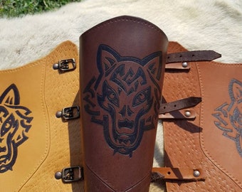 May include: Two leather arm guards with wolf head designs. One is brown and the other is tan. Both have buckles and straps.