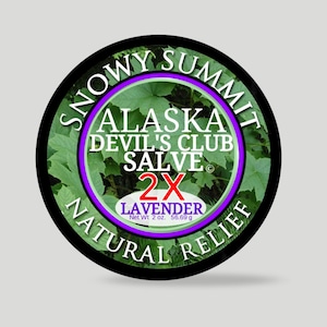 May include: A circular label with a black border, displaying the text "SNOWY SUMMIT ALASKA DEVIL'S CLUB SALVE 2X LAVENDER NATURAL RELIEF." The design includes a green background with leaf patterns and a purple inner circle. Net weight is 56.69 g.