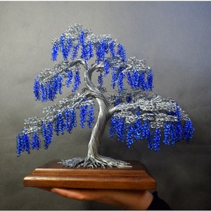 May include: A wire sculpture of a tree with blue beads representing blossoms. The tree is on a wooden base.