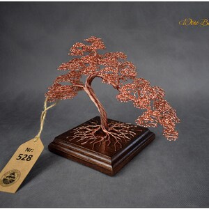 May include: A copper wire bonsai tree sculpture with a brown wooden base. The tree is shaped like a weeping willow and has a tag with the number 528 on it.
