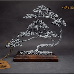 K&ouml;nnte beinhalten: Handgefertigte Draht-Bonsai-Baumskulptur. Der Baum besteht aus silberfarbenem Draht und ist auf einem dunklen Holzsockel montiert. Die Skulptur hat ein Etikett mit der Aufschrift "Nr. 863". Die Worte "Wire Bonsai Art" sind kursiv geschrieben.
