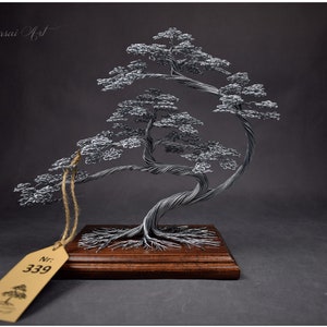 K&ouml;nnte beinhalten: Handgefertigte Draht-Bonsai-Baumskulptur. Der silberfarbene Baum ist auf einem gebeizten Holzsockel montiert. Ein Anh&auml;nger mit der Nummer 339 h&auml;ngt an der Skulptur. Die Worte "Wire Bonsai Art" sind im Hintergrund zu sehen.