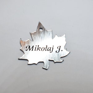 May include: Silver maple leaf-shaped tag with the name "Mikołaj J." engraved on it.