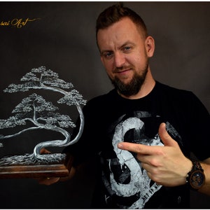 K&ouml;nnte beinhalten: Handgefertigte Draht-Bonsai-Baumskulptur. Der Baum hat ein silberfarbenes Drahtdesign mit detailliertem Laub, montiert auf einem Holzsockel. Das Kunstwerk ist mit "Wire Bonsai Art" und "Unique Handmade" gekennzeichnet.