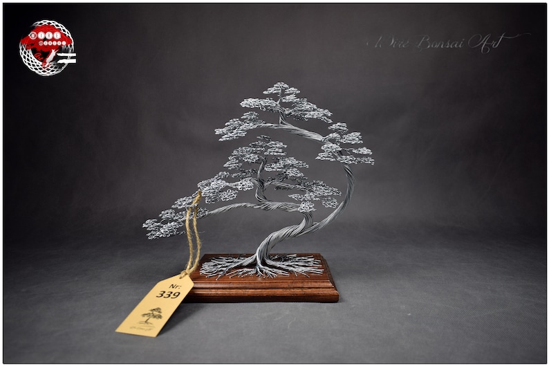 K&ouml;nnte beinhalten: Silberdraht-Bonsai-Baumskulptur mit verdrehtem Stamm und geschichtetem Laub, montiert auf einem Holzsockel. Die Skulptur hat ein Etikett mit der Nummer 339. Der Hintergrund ist dunkelgrau.